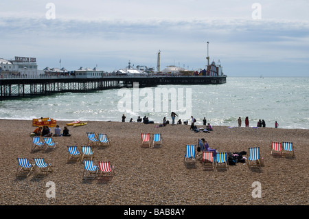 Blick über einen Kiesstrand, übersät mit Liegestühlen in Richtung Brighton Pier. Stockfoto