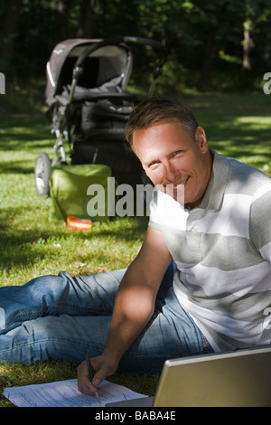 Ein Mann mit einem Kinderwagen und einem Computer in einem Park einen sonnigen Tag Schweden. Stockfoto