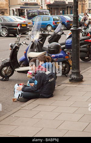 Ein junges Paar von Studenten auf dem Bürgersteig sitzen und Essen, Broad Street, Oxford Stockfoto