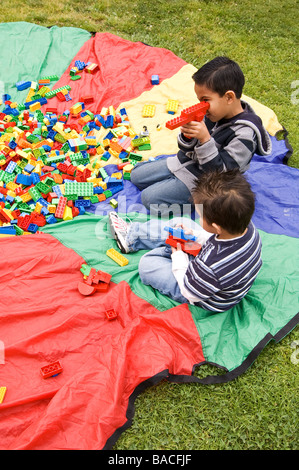 Zwei lateinische Kinder sitzen auf einem Fallschirm mit Legos spielen in einem park Stockfoto