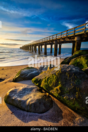 Eine große hölzerne Pier bei Sonnenuntergang mit Steinen bedeckt alle grünes Moos mit schönen goldenen Licht beleuchtet Stockfoto