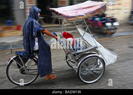 Schwenken. Straßenszene. Cyclo-Fahrer mit blauen Regenmantel unter dem Regen in Vietnams Hauptstadt Hanoi Stockfoto