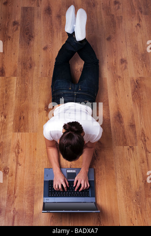 Junge Frau in Freizeitkleidung liegend auf einem Holzfußboden mit einem Laptopcomputer Stockfoto