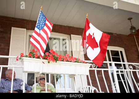 Älteres Paar auf Veranda mit amerikanischen und kanadischen Flaggen Stockfoto