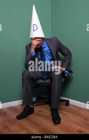 Geschäftsmann, saß auf einem Stuhl in der Ecke einen Dunce Hut Stockfoto