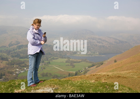 Junge Frau sucht ein Handy-Signal beim stehen auf einem Berg in ländlicher Umgebung Stockfoto