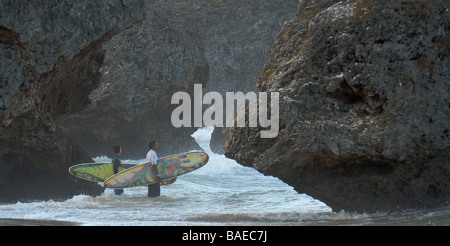 Zwei Surfer zwischen hohen Felsen stehend mit Blick auf das Meer vor dem Surfen Stockfoto
