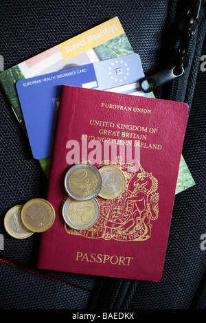 Nahaufnahme eines britischen Passes, Gesundheitskarte EHIC und einige ausländische Währung sitzt oben auf dem Koffer Stockfoto