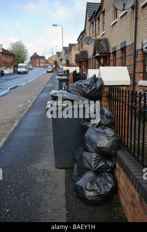 Plastiktüten stapelten sich neben einer überquellenden schwarz bin zur Abholung bereit. Stockfoto