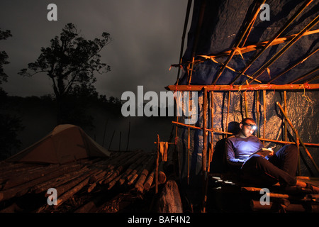 Männlichen Höhlenforscher liest ein Buch spät in der Nacht in seinem abgelegenen Dschungel-Camp im Herzen von einer Insel namens New Britain Stockfoto