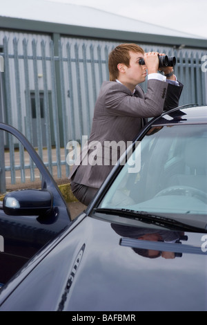 Junger Mann stützte sich auf Auto durch ein Fernglas suchen Stockfoto