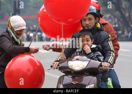 Vietnamesische Familie auf einem Motorrad kaufen einen Ballon von einem Straßenhändler in Hanoi Vietnam Stockfoto