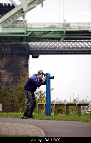 Einsamer Teenager überblickt durch ein mock Teleskop den Fluss Mersey in Runcorn unter Silver Jubilee Bridge Stockfoto