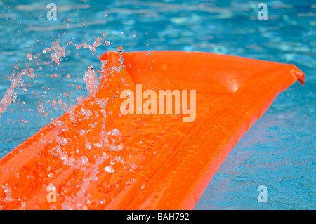 Spritzwasser über eine orange Luftmatratze schwimmend in einem Schwimmbad. Stockfoto