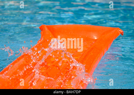 Spritzwasser über eine orange Luftmatratze schwimmend in einem Schwimmbad. Stockfoto