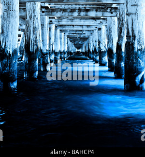 Langen, dunklen Tunnel unter dem hölzernen Pier von tief blau und kaltem Meerwasser überflutet. Nostalgische Licht und Schatten. Stockfoto