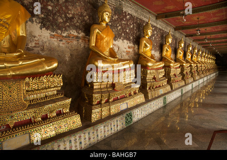 Gold Buddhastatuen säumen die Galerien, die umschließen das Hauptgebäude im Wat Suthat in Bangkok Thailand Stockfoto