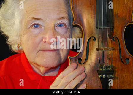 Porträt der älteren Frau ist in rot mit einer alten Geige Stockfoto