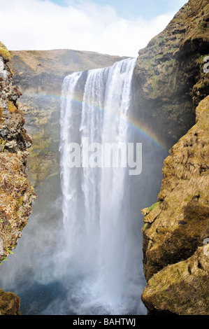 Vorderansicht der Skogafoss Wasserfall, Tauchbecken und Regenbogen, durch einen Spalt in der Spaziergang auf der Seite, Southern Island Felsen Stockfoto