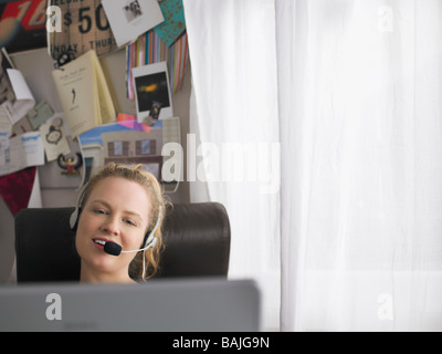 Frau mit Laptop tragen Kopfhörer sitzen am Schreibtisch Stockfoto