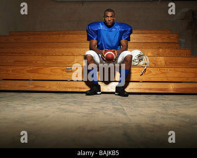 American Footballspieler sitzen auf Bank Holding Ball, Porträt Stockfoto