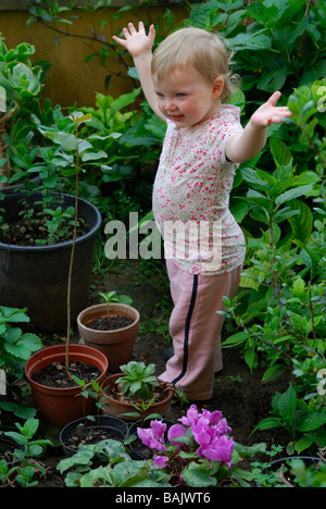 16 Monate altes Babymädchen imitiert, ein Baum wächst Stockfoto