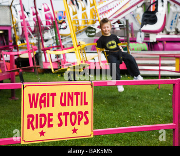 Glückliche junge Spaß auf einem Messegelände fahren. Schaukeln und Karussells. VEREINIGTES KÖNIGREICH. Warnschild warten bis Fahrt stoppt. Stockfoto