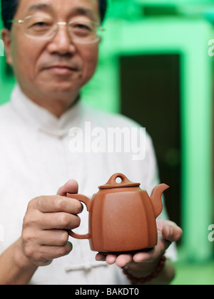 Ein chinesischer Mann zeigt eine kleine Terrakotta farbigen Teekanne. Stockfoto