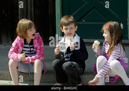 Drei Kinder, junge und zwei Mädchen essen und Eistüten genießen und entspannen, reden Stockfoto