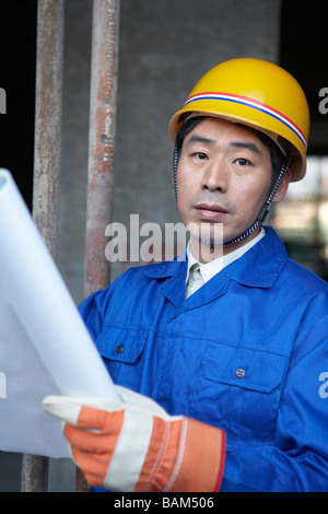 Mann In Baustelle trägt einen Schutzhelm und hält Blaupausen Stockfoto