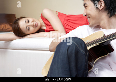 Junges Paar zu faulenzen, während der Mann Gitarre spielt Stockfoto