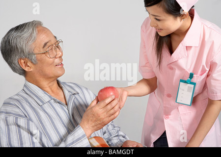 Krankenschwester geben einen Apfel für den Menschen Stockfoto