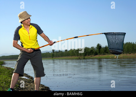 Mann steht am Ufer eines Sees ein Fisch In seinem Netz gefangen Stockfoto