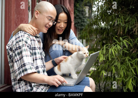 Junges Paar Blick auf Laptop, Mann klopfte Katze Stockfoto