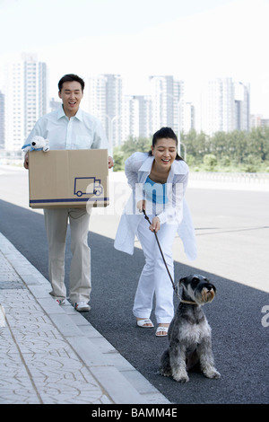 Mann trägt eine große Kiste, während Frau auf eine Hundeleine hält Stockfoto
