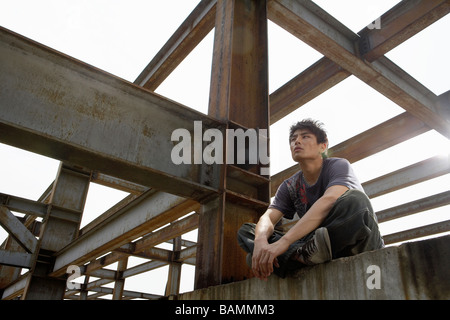 Junger Mann sitzt auf einem Balken In einer Baustelle Stockfoto