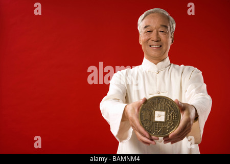 Älterer Mann, der riesige chinesische Münze hält Stockfoto