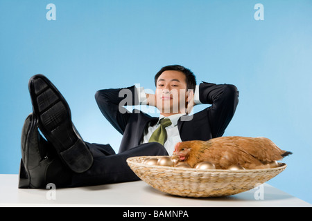 Geschäftsmann entspannende neben Huhn und goldenen Eiern Stockfoto