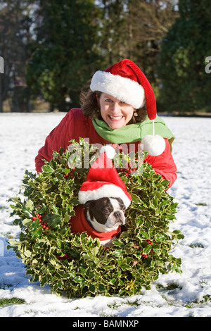 Frau in einem Park mit einem Hund trägt einen Weihnachtskranz Stockfoto