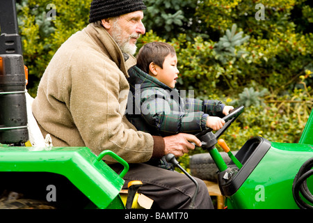 Junge, einen Traktor zu fahren, mit Unterstützung der männlichen Erwachsenen Stockfoto