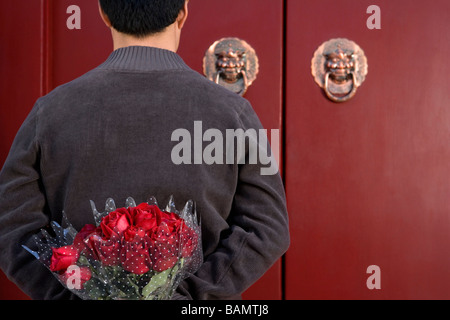 Junger Mann warten an der Haustür mit einem Rosenstrauß hinter seinem Rücken Stockfoto