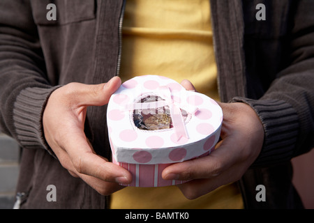 Junger Mann hält eine Schachtel Pralinen Stockfoto