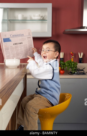 Kleiner Junge liest eine Zeitung am Frühstückstisch Stockfoto