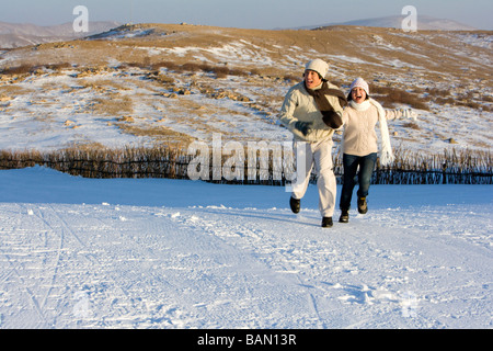 Junger Mann und junge Frau läuft im Schnee Stockfoto