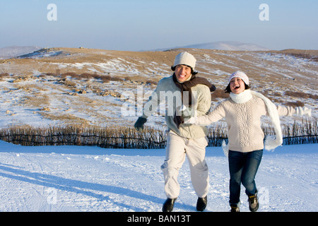 Junger Mann und junge Frau läuft im Schnee Stockfoto
