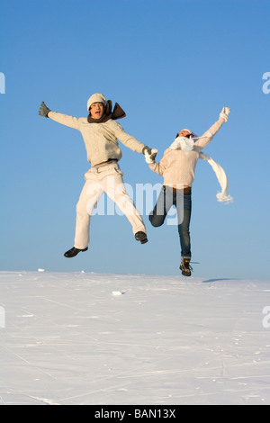 Junger Mann und junge Frau, die einen Sprung über eine Schneelandschaft Stockfoto