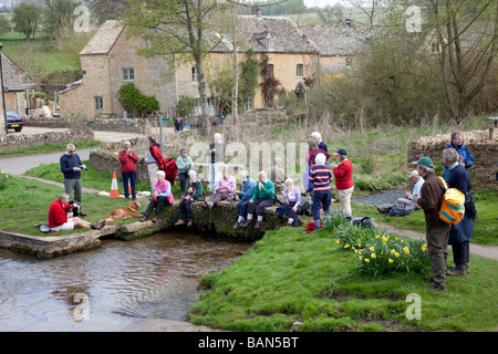 Gruppe senior Rucksacktouristen Mittagessen brechen durch die Furt am Fluss Auge Cotswolds UK Stockfoto