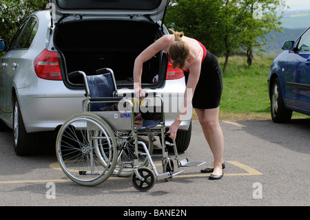 Frau zu errichten und die Zusammenstellung eines Rollstuhls mit Auto in einen behinderten Parkplatz geparkt Stockfoto