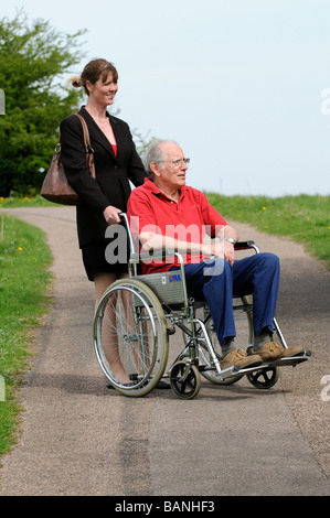 Weibliche Pflegeperson drängen älteren Mann im Rollstuhl auf dem englischen Land UK Stockfoto