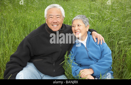 Hochrangige asiatische paar sitzt in hohe Gräser lächelnd Stockfoto